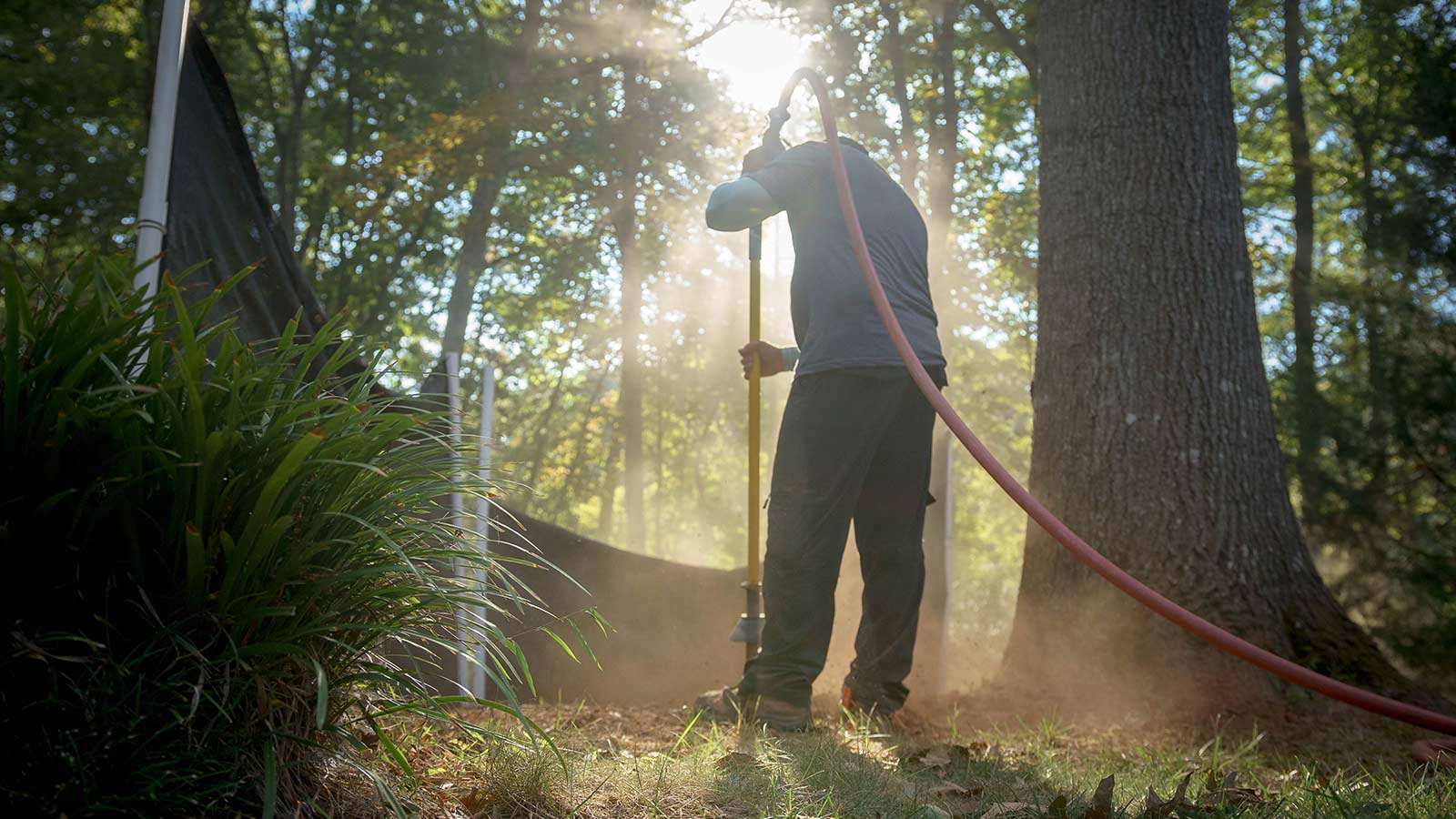 Air spading equipment loosening compacted soil beneath a tree to inject compost